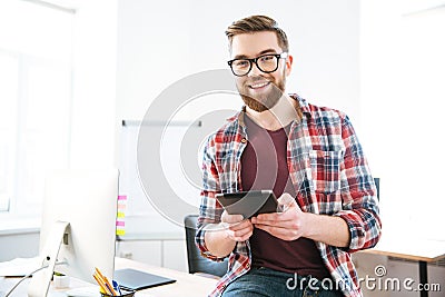 Cheerful male sitting and holding tablet in the office Stock Photo