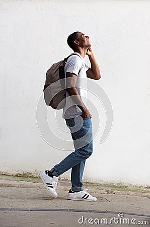 Cheerful male student walking and talking on cell phone Stock Photo