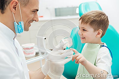 Cheerful man dentist demonstrating tooth brushing to little boy Stock Photo