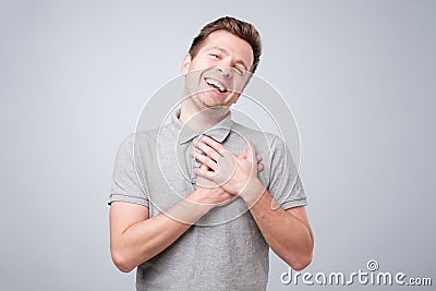 Cheerful man smiles happily, keeps hands on chest. Pleased male glad to recieve compliment from woman. Stock Photo
