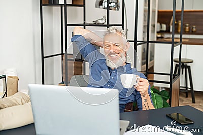 Cheerful mature male employee enjoys morning coffee at the workplace in the office Stock Photo