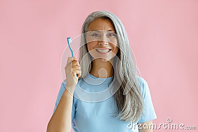 Cheerful middle aged Asian woman holds toothbrush standing on pink background Stock Photo