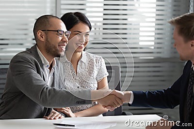 Cheerful mixed race married spouse shaking hands with real estate agent. Stock Photo