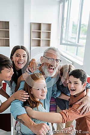 cheerful multicultural teenagers embracing laughing teacher Stock Photo