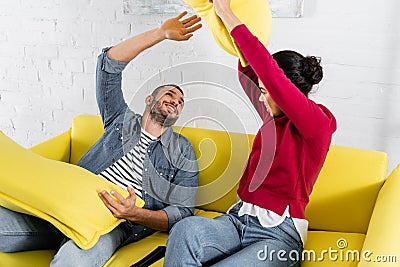 Cheerful multietnic couple pillow fighting near Stock Photo