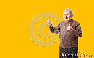 Cheerful octogenarian woman wearing brown sweater showing on empty place for copy space. Stock Photo