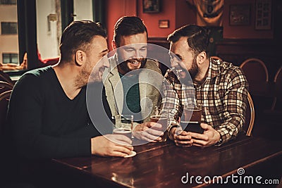 Cheerful old friends having fun and drinking draft beer in pub. Stock Photo