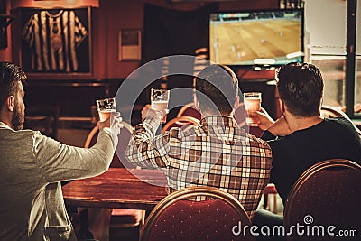 Cheerful old friends watching sports and drinking draft beer in pub. Stock Photo