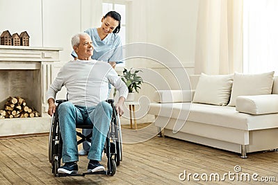 Cheerful positive caregiver moving a wheelchair Stock Photo