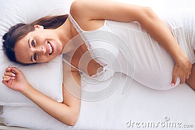 Cheerful pregnant woman lying on white sheet in bed Stock Photo