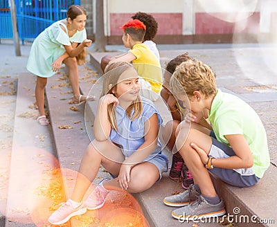 Cheerful preteen girls and boys sitting on steps outdoors and chatting Stock Photo