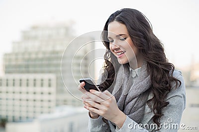 Cheerful pretty brunette in winter clothes sending a text on her Stock Photo