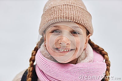 Cheerful pretty girl in warm woolen winter cap and scarf looking at camera Stock Photo
