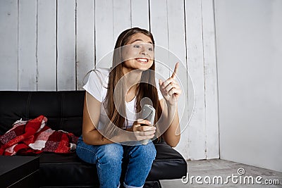 Cheerful pretty girl watching tv, sitting on sofa at home. Stock Photo