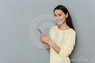 Cheerful pretty young woman standing and using cell phone Stock Photo