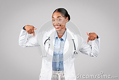Cheerful professional young black doctor point fingers down at copy space, recommends ad and offer Stock Photo