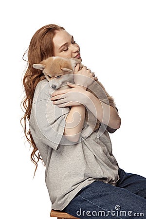 Cheerful redhead young girl with long curly hair holding cute little puppy of corgi dog isolated on white background Stock Photo
