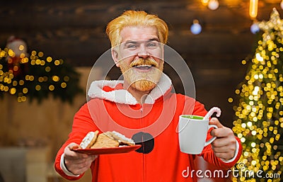 Cheerful Santa Claus with cookies and cup of coffee. New year advertising. Happy Bearded man in Santa costume. Stock Photo