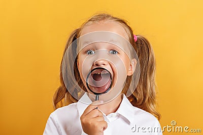 Cheerful schoolgirl little girl shows teeth and smiles through a magnifying glass. Stock Photo