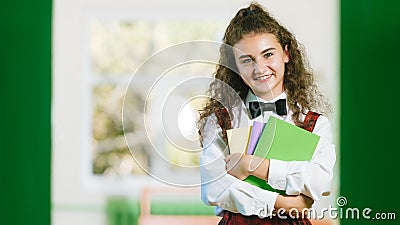 Cheerful schoolgirl in school uniform standing in the hallway with books Stock Photo