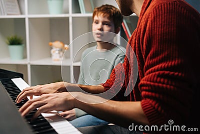 Cheerful schoolkid boy sings song with music teacher playing piano at home during lesson. Stock Photo