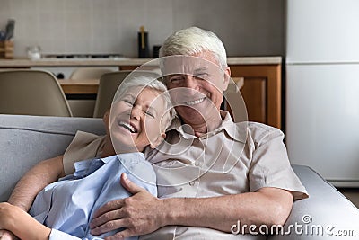 Cheerful senior couple relaxing on home couch, hugging with love Stock Photo