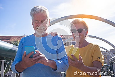 Cheerful senior couple walking on a bridge in the city. Looking at their own mobile phone and smiling. Elderly modern and Stock Photo