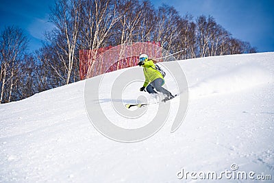 Cheerful skier girl in green jacket in front of snowy mountains Stock Photo