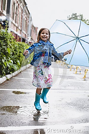 Cheerful small girl having fun in puddle on street Stock Photo