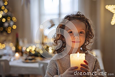 Cheerful small girl standing indoors at Christmas, holding candle. Stock Photo