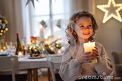 Cheerful small girl standing indoors at Christmas, holding candle. Stock Photo