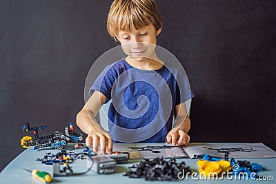 Cheerful smart schoolboy sitting at the table and constructing a robotic device at home Stock Photo