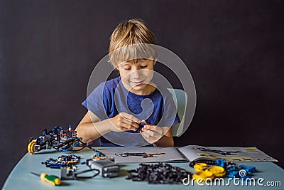 Cheerful smart schoolboy sitting at the table and constructing a robotic device at home Stock Photo