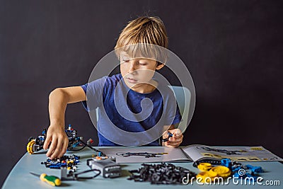 Cheerful smart schoolboy sitting at the table and constructing a robotic device at home Stock Photo