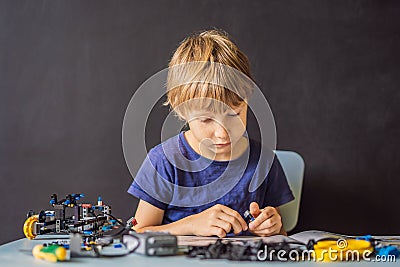 Cheerful smart schoolboy sitting at the table and constructing a robotic device at home Stock Photo