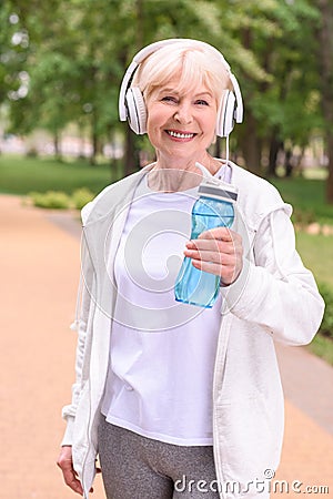 cheerful sportswoman with bottle of water and headphones standing in park Stock Photo