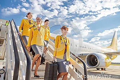 Cheerful stewardesses walking down airplane stairs under cloudy sky Stock Photo