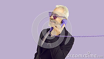 Cheerful stylish and charismatic senior man talking on landline phone on purple background. Stock Photo