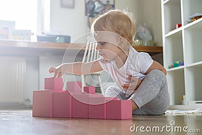 Cheerful toddler arrangement pink cubes assembling tower educational Maria Montessori materials Stock Photo