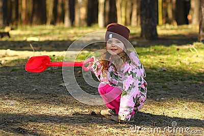 Cheerful todler girl showing the way in the forest with a red shovel Stock Photo