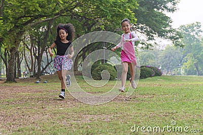 Cheerful two little kids having fun while running through grassy field with tree and racing against each other. Cute girl enjoying Stock Photo