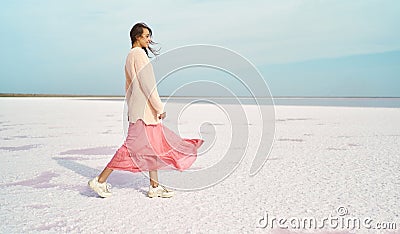 Cheerful walking woman in sweater and blowing dress at paradise white coast of pink lake Stock Photo