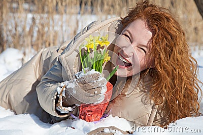 Cheerful woman lying on snow surface with yellow narcissuses in hand Stock Photo