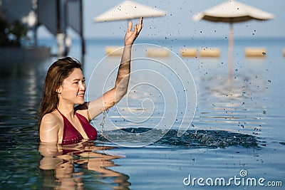 Cheerful woman in swimsuit playing water splashing in swimming pool with sea background Stock Photo