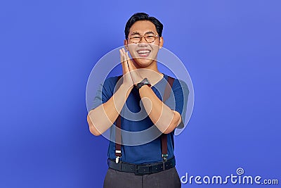 Cheerful young Asian man with hands on cheeks and wearing glasses on purple background Stock Photo