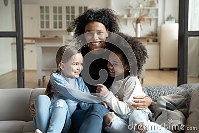 Cheerful African mother sitting on couch embraces multiracial daughters Stock Photo