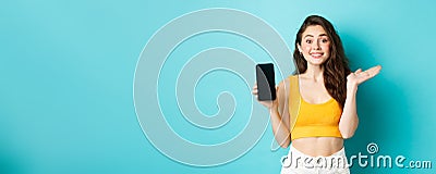 Cheerful young girl introduce your app or store, showing emtpy smartphone screen and smiling at camera, standing against Stock Photo