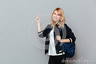 Cheerful young lady student with backpack pointing Stock Photo