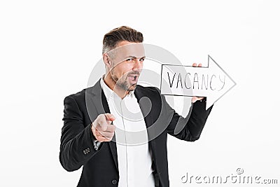 Cheerful young man in black jacket gesturing on camera with finger while holding speech arrow pointer with word vacancy, isolated Stock Photo