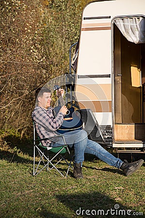 Cheerful young man playing on his guitar in front of his retro camper van Stock Photo
